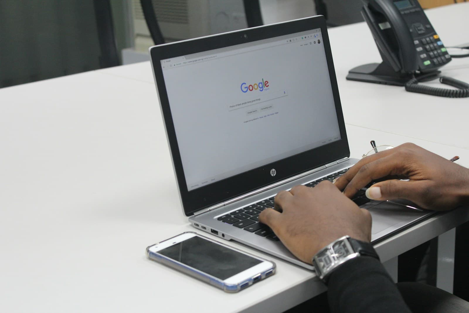 Hands typing on a laptop with a phone on the desk