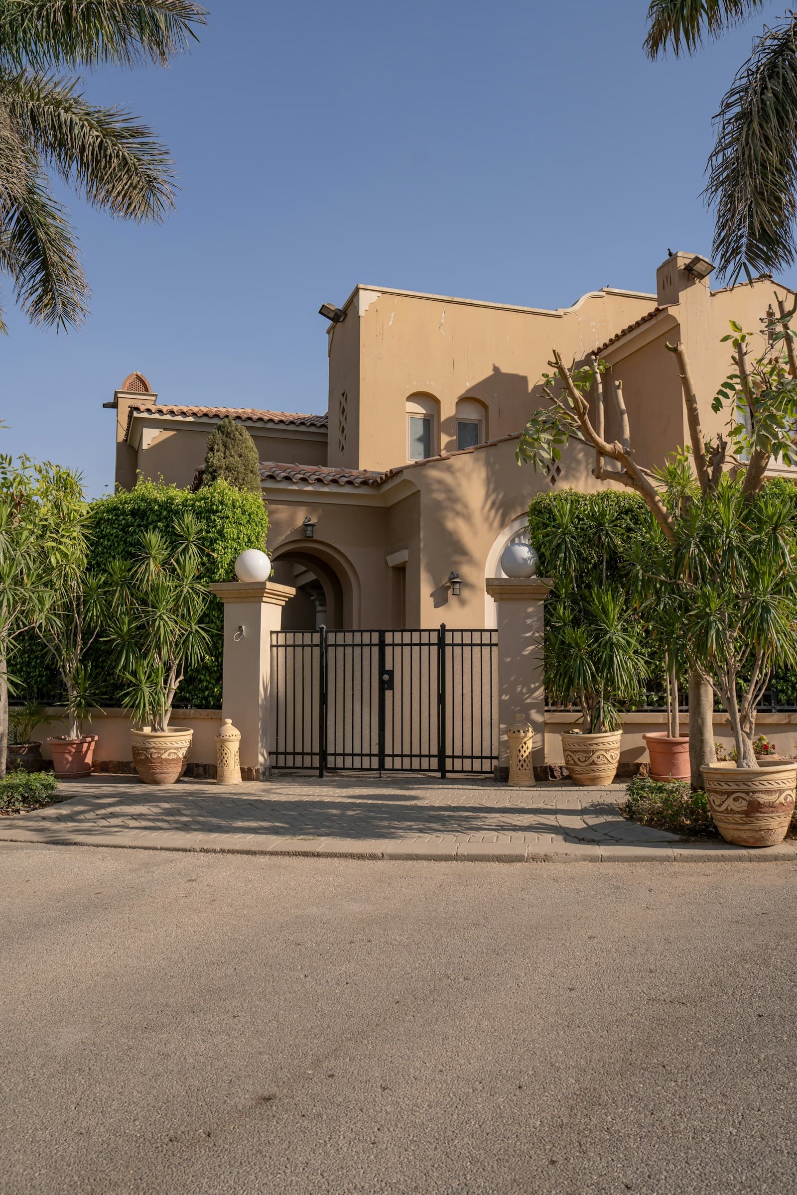 A gated house behind palm trees on a quiet estate road